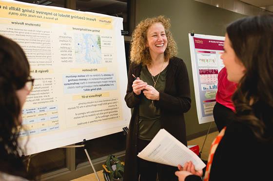 Photo of a smiling woman in front of a poster presentation, speaking with two women facing her